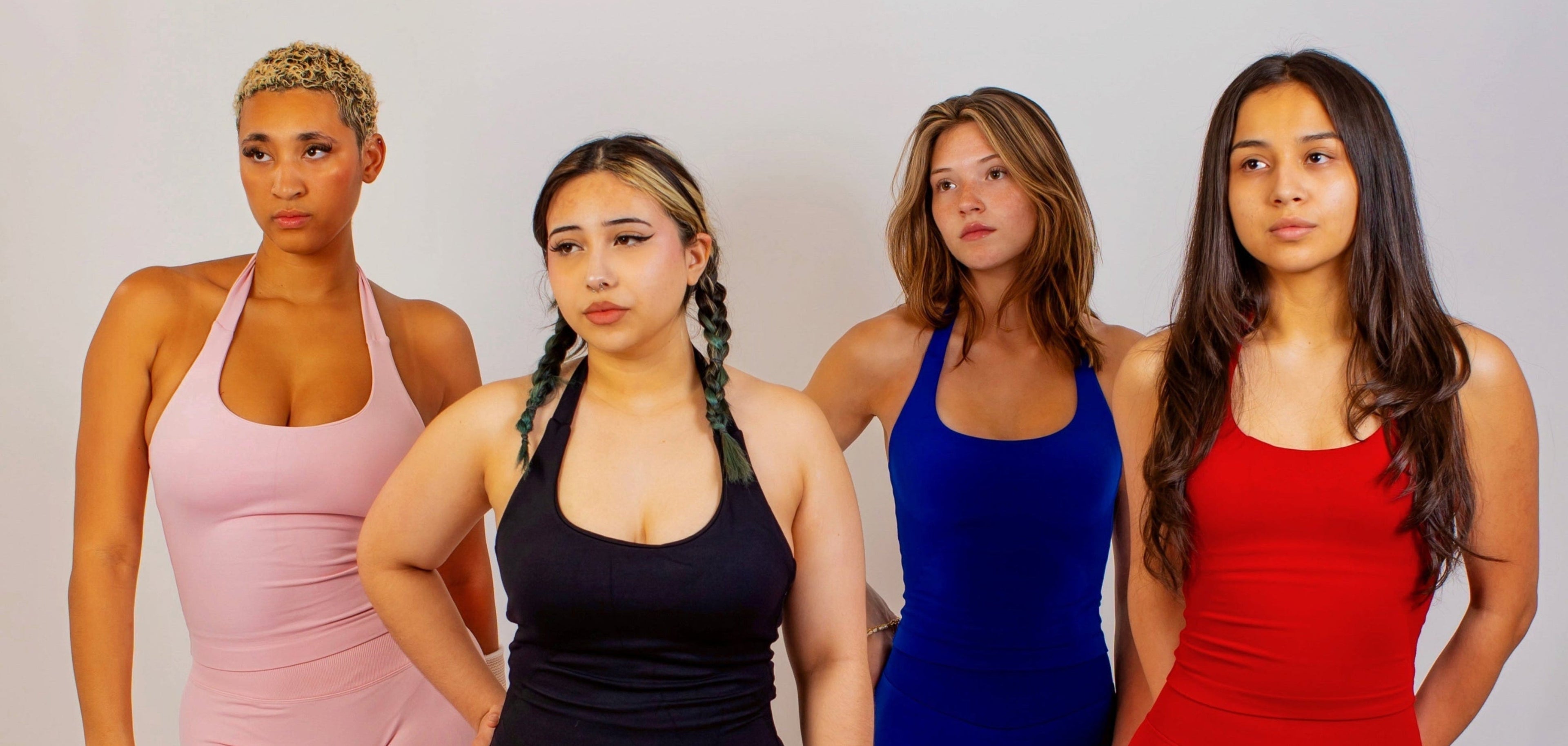 Four women wearing colorful one-piece swimsuits on a plain background